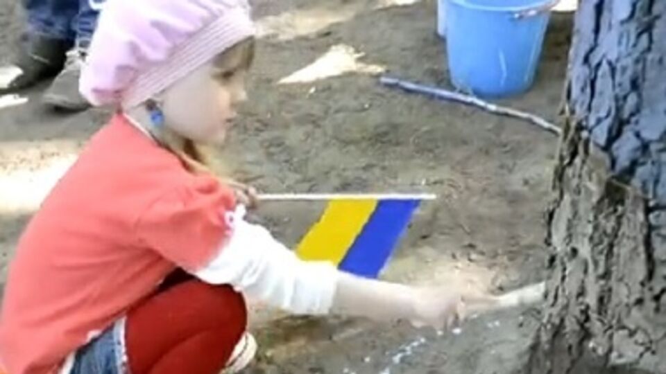 Девочка красит дерево в родном Луганске в цвета флага Украины