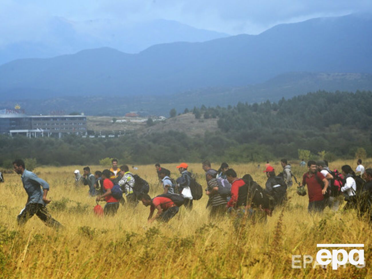 Мигранты, прорвавшиеся через колючую проволоку, бегут по полю в сторону македонского города Гевгелия