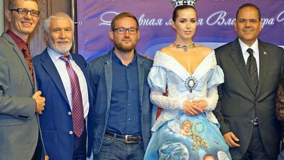 В руке глава России держит Землю, а сзади на платье нарисован храм Василия Блаженного