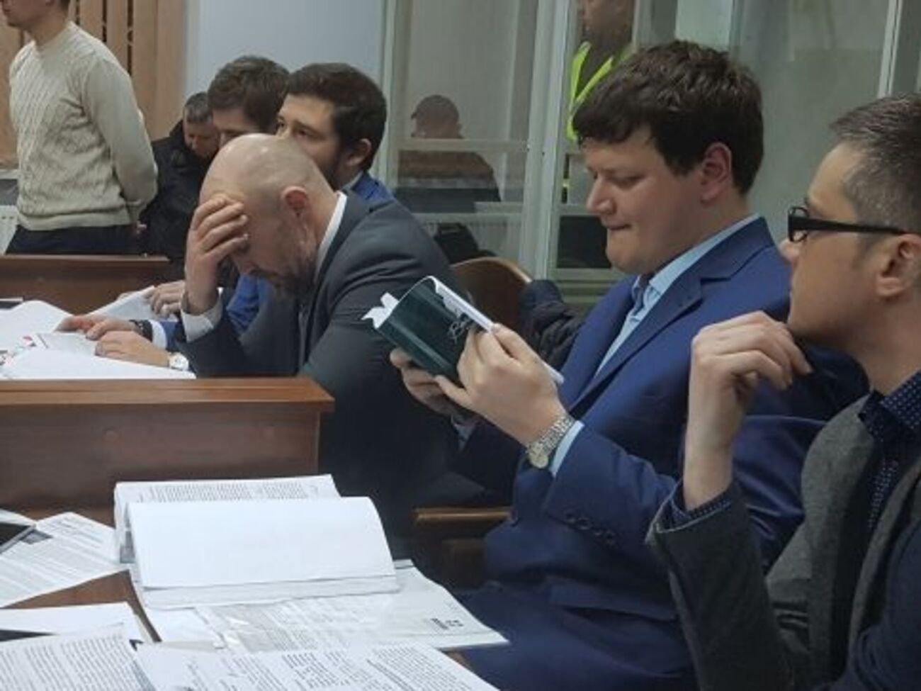 Мангера (на фото з похиленою головою) захищає п'ятеро адвокатів