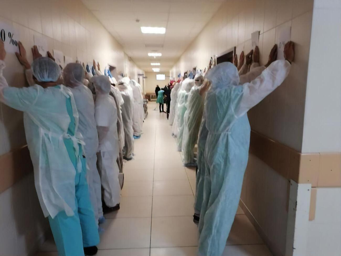 Лікарі та журналісти вишикувалися вздовж стін обличчям до стіни з піднятими руками й аркушами паперу з написом "0%"