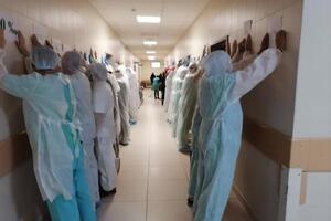 Лікарі та журналісти вишикувалися вздовж стін обличчям до стіни з піднятими руками й аркушами паперу з написом "0%"
