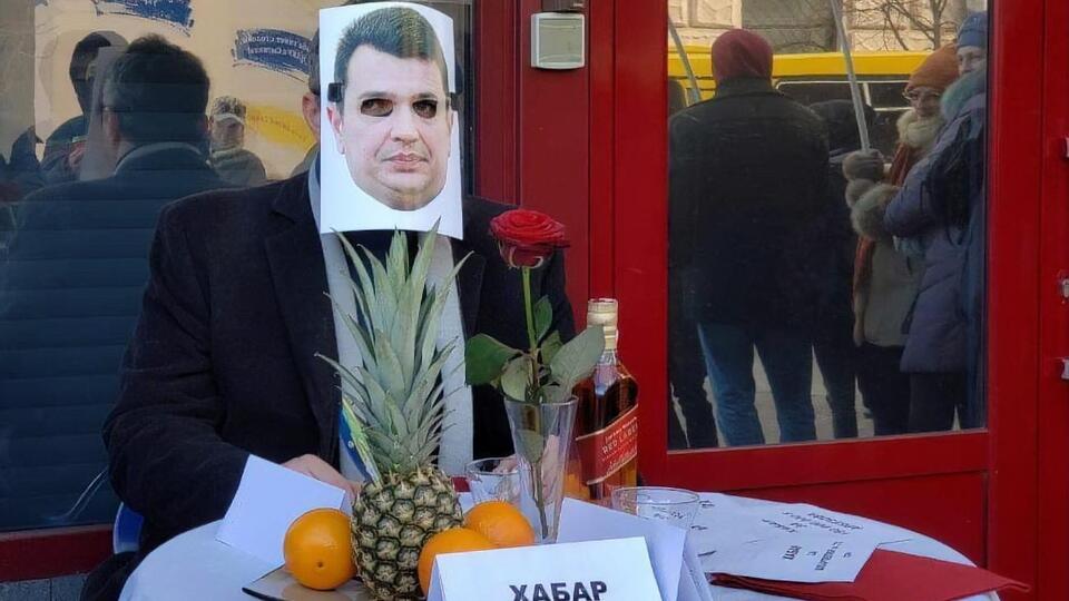 Біля входу в НАБУ за столом з екзотичними фруктами і напоями сидить активіст у масці з обличчям Ситника