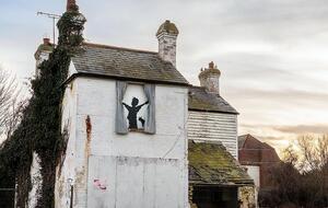 Бэнкси изобразил на заколоченном фанерой окне дома мальчика с разведенными руками, который якобы раздвигает занавески из смятых листов металла