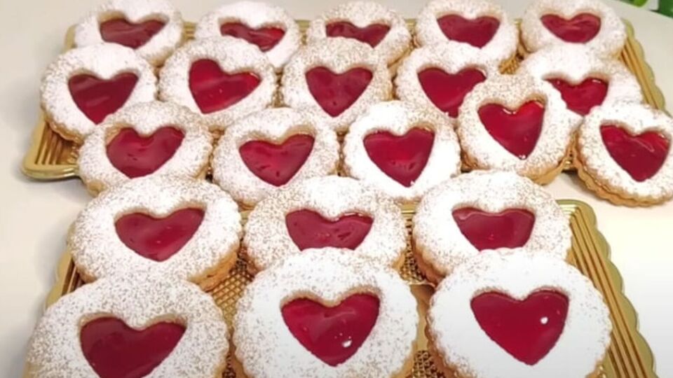Целое печенье смажьте джемом и сверху на него выложите печенье с сердцами, посыпанное сахарной пудрой