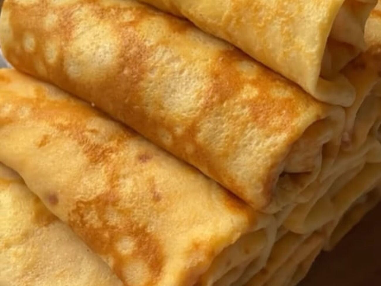 Смажьте каждый блинчик крем-сыром, выложите кусочки ветчины, твердого сыра и скрутите рулетом