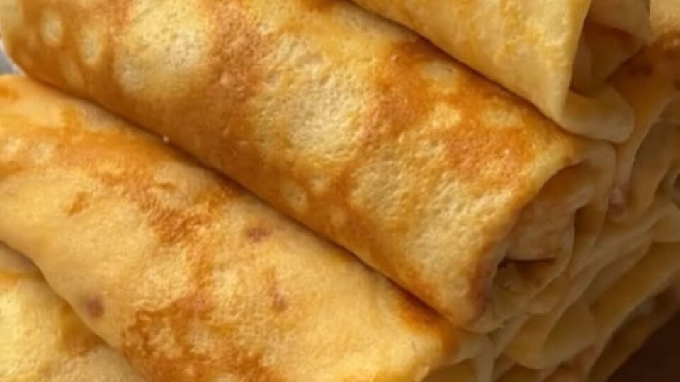 Змастіть кожен млинець крем-сиром, викладіть шматочки шинки, твердого сиру і скрутіть рулетом